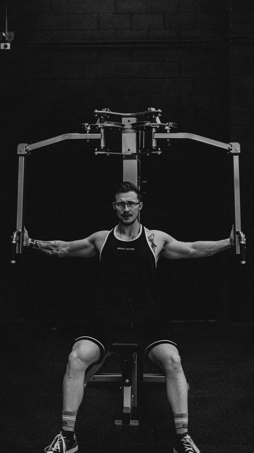 A man training on a pec deck machine in a dark gym, shot in black and white